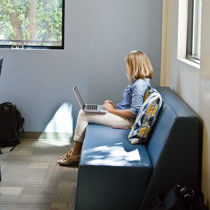 Woman sitting on a couch at the Thought Design learning lab with a laptop 