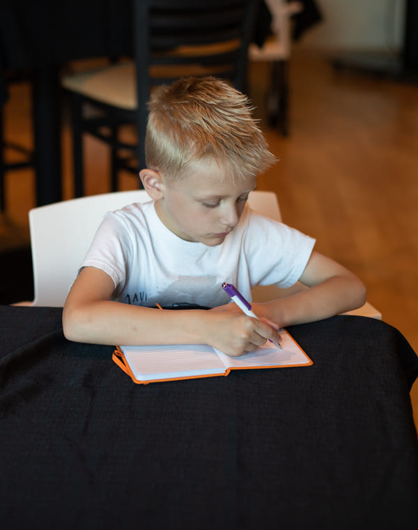 Young boy sitting at a desk, writing in a notebook