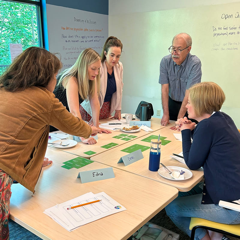 People standing in a group pointing and discussing notes on a table at a Thought Design workshop