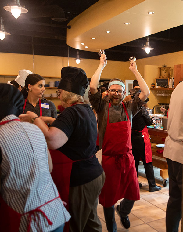 Chef Shaun with hands in the air walking among cooking class attendees
